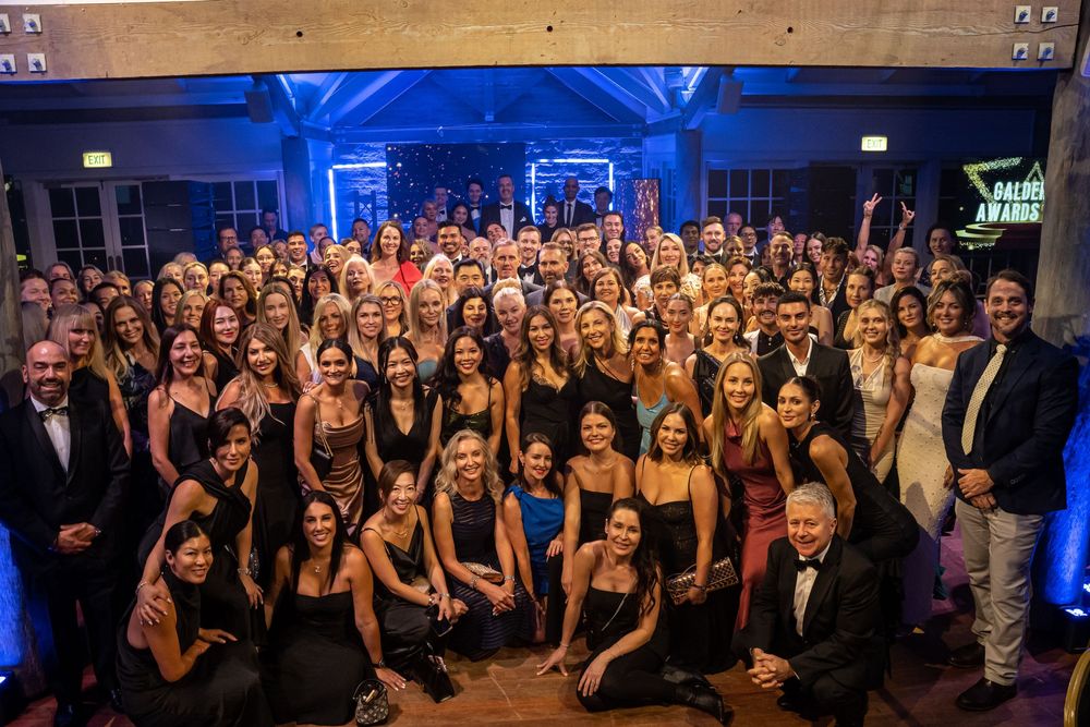A panoramic view of a formal event shows a large group gathered in an elegant venue with blue accent lighting.