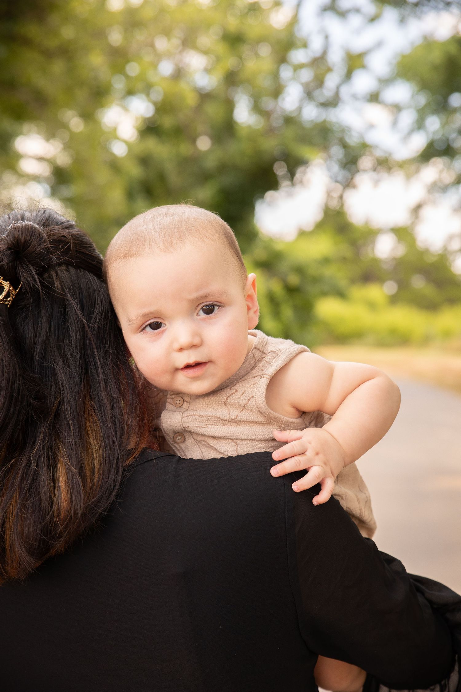 A baby in beige clothing peeks over a shoulder in a series of outdoor portrait shots with natural lighting and bokeh background.
