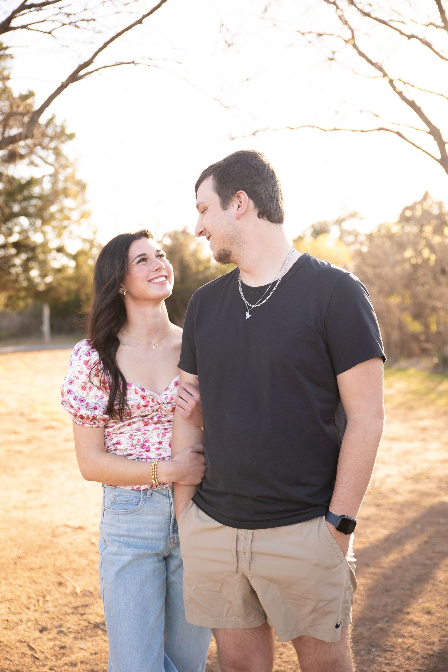 A couple embraces during a golden hour photoshoot in a field with warm sunlight creating a romantic atmosphere.