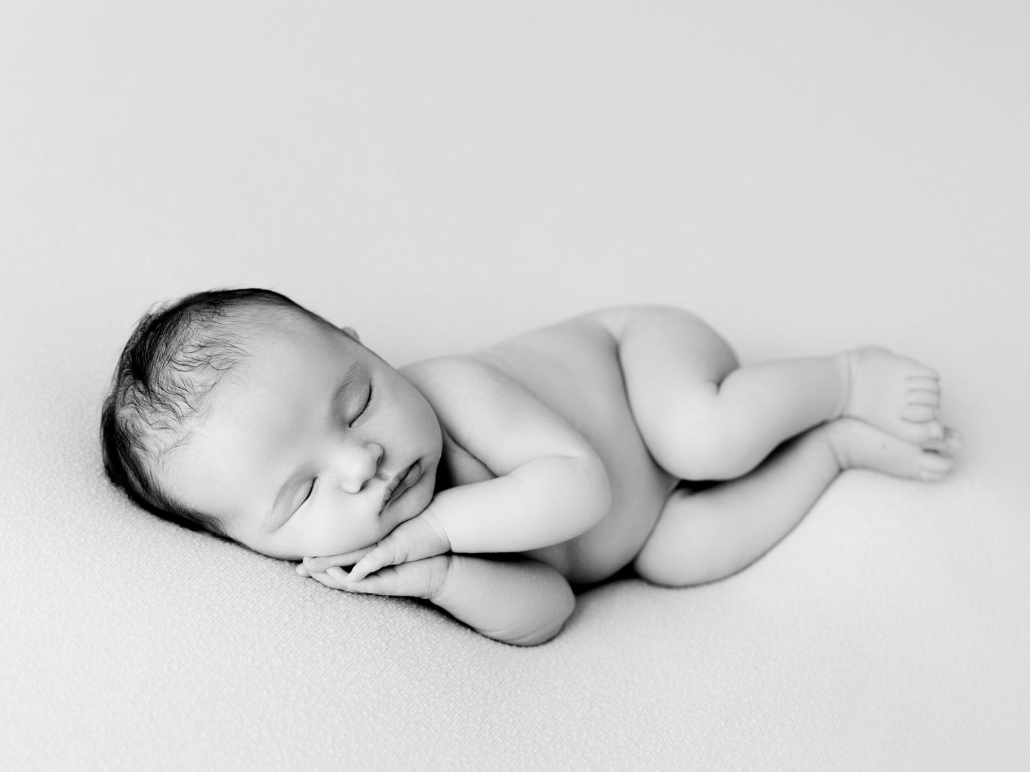 Sleeping newborn baby wearing delicate floral headband wrapped in soft gray blanket against white background.