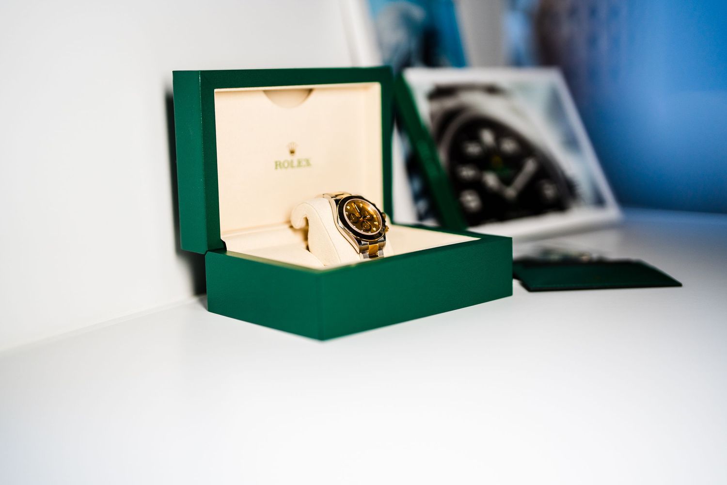 Luxury green watch box with gold accents sits against blurred blue background.