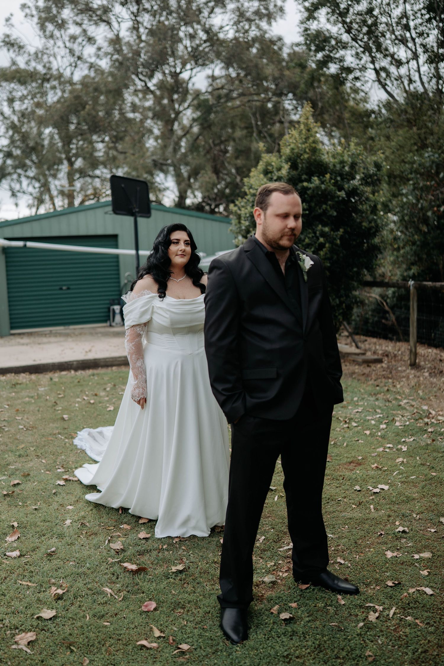 A couple in wedding attire share an intimate embrace outdoors during their special day.