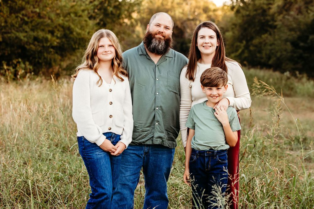 Family in coordinating green and white outfits poses together in a sunlit field at golden hour.