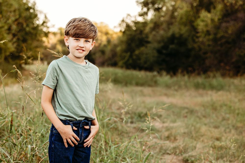 A child in a sage green t-shirt plays in a golden sunlit field during sunset.