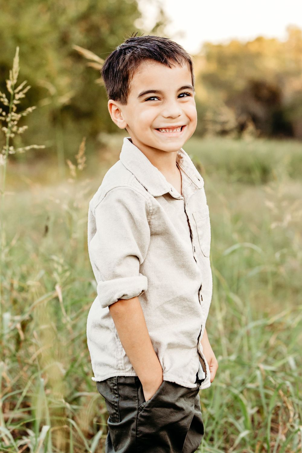 A young child in a light colored shirt poses playfully in a grassy field at sunset.
