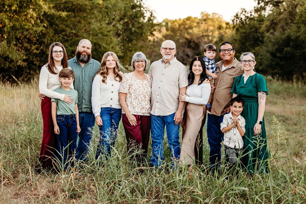 A group of people wearing casual clothing pose together outdoors in a grassy field at sunset.