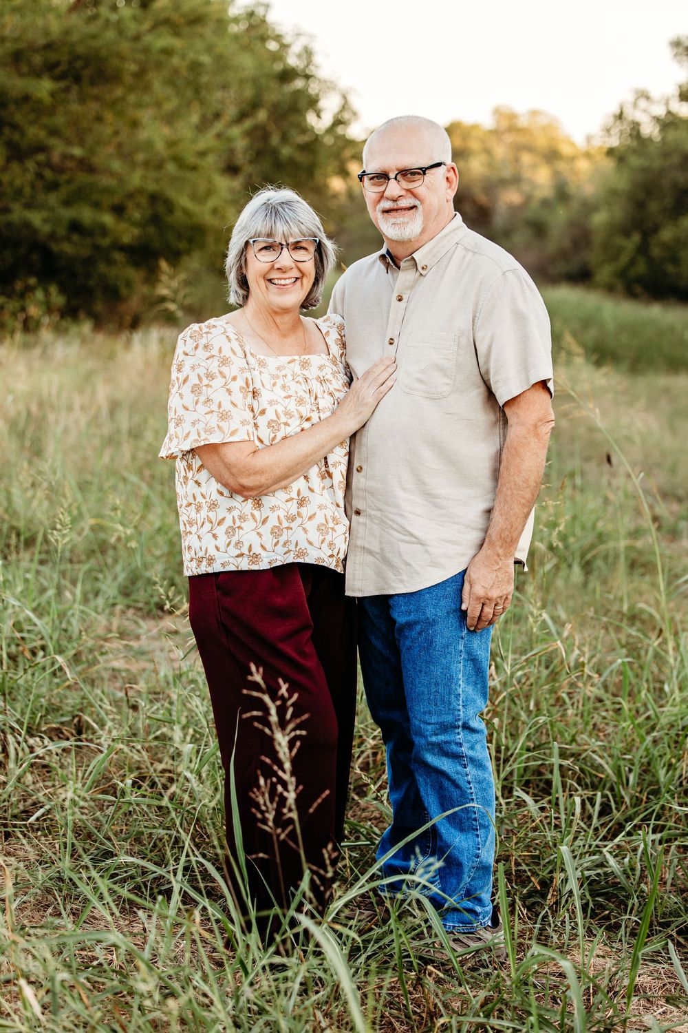An affectionate couple stands together in a natural field setting during golden hour.