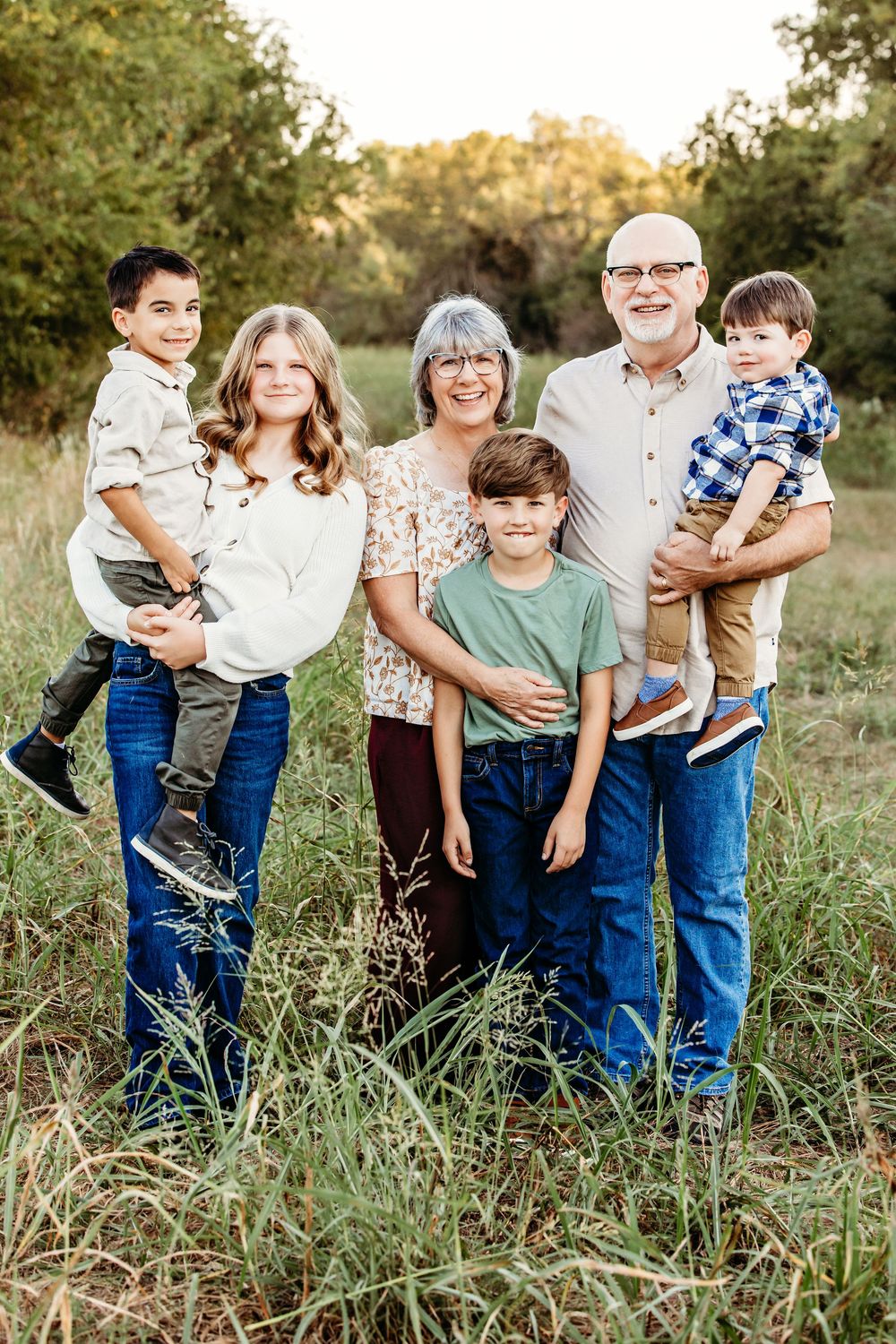 A family group poses together in a grassy field during a golden hour outdoor photo session.