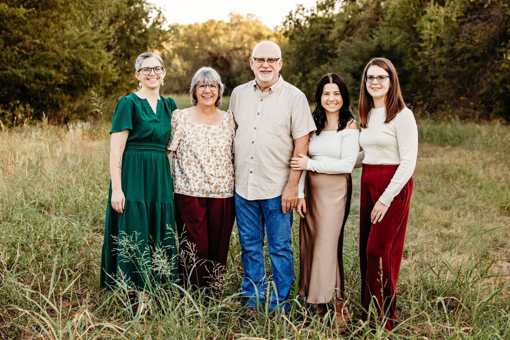 A large family group poses together in a grassy field during golden hour sunset.