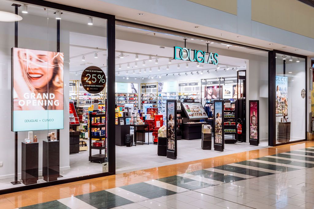 A modern shopping mall interior with white walls, tiled floors and retail storefronts stretching down a long corridor.