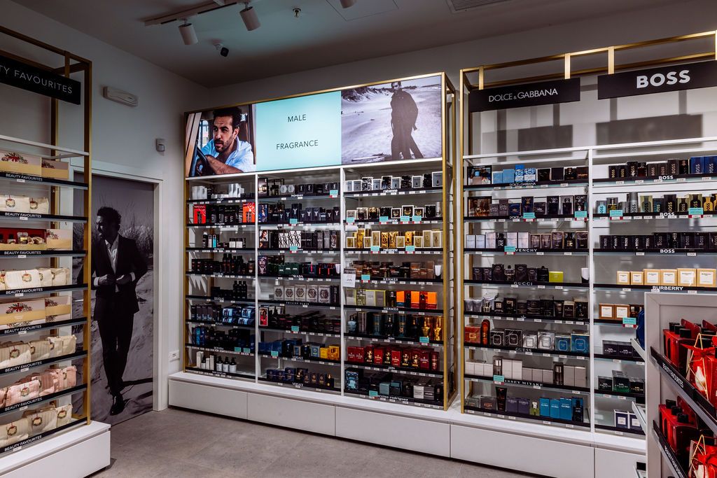 Modern retail store interior displaying rows of perfume bottles and fragrances on illuminated glass shelves along white walls.