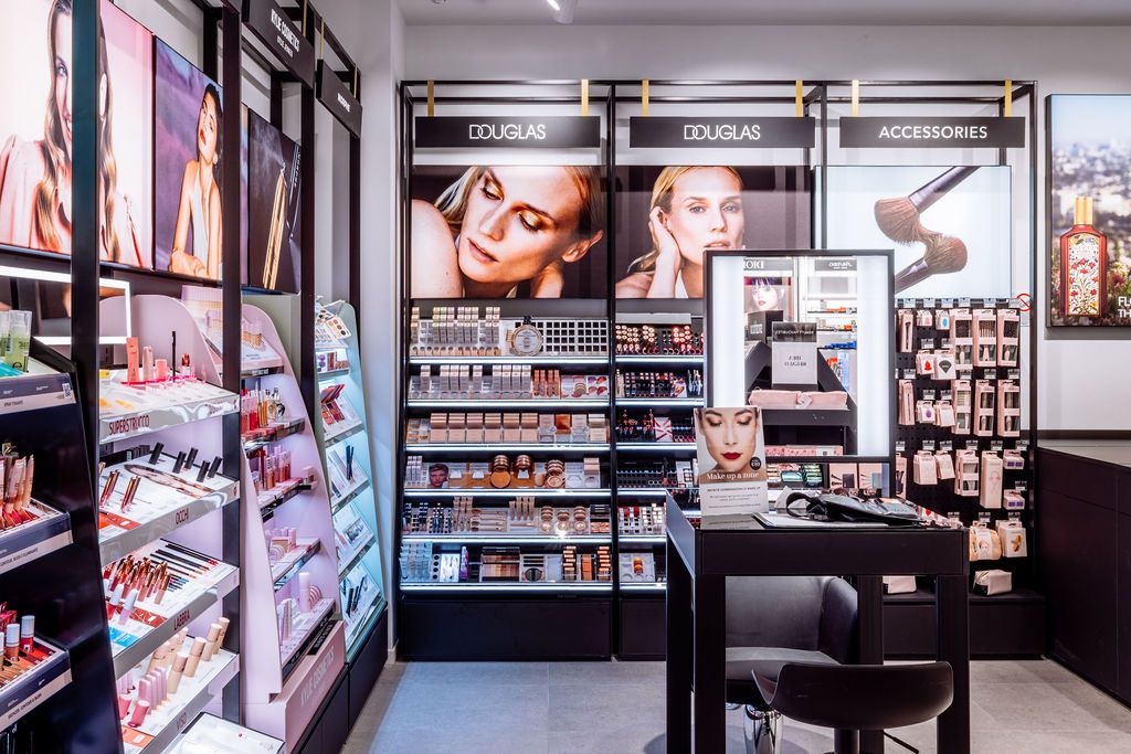 Beauty store interior with black shelving units displaying cosmetics, makeup testers, and promotional beauty photography.