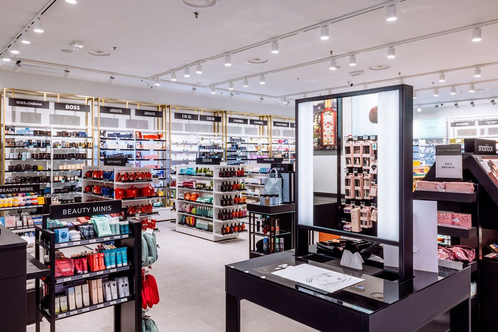 Modern retail electronics store interior with shelves of products and digital displays under bright lighting.