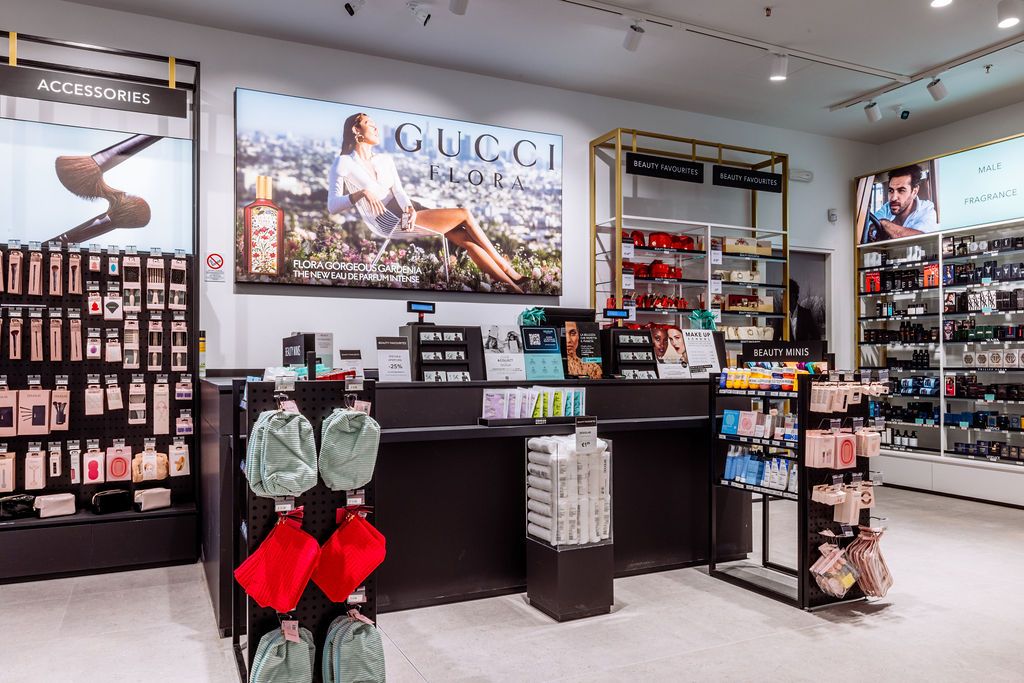 Cosmetics retail counter with large fashion advertisement display and product shelves in bright store setting.