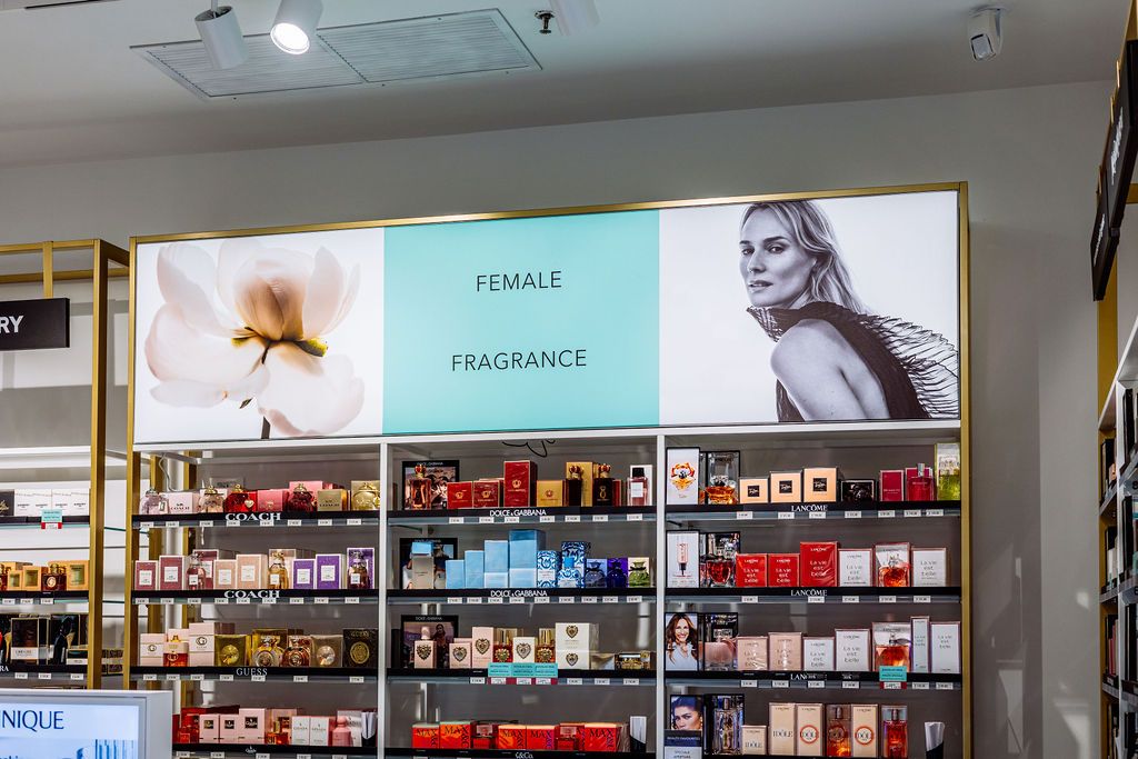 Interior view of a retail store showing long shelves stocked with perfume and fragrance products.