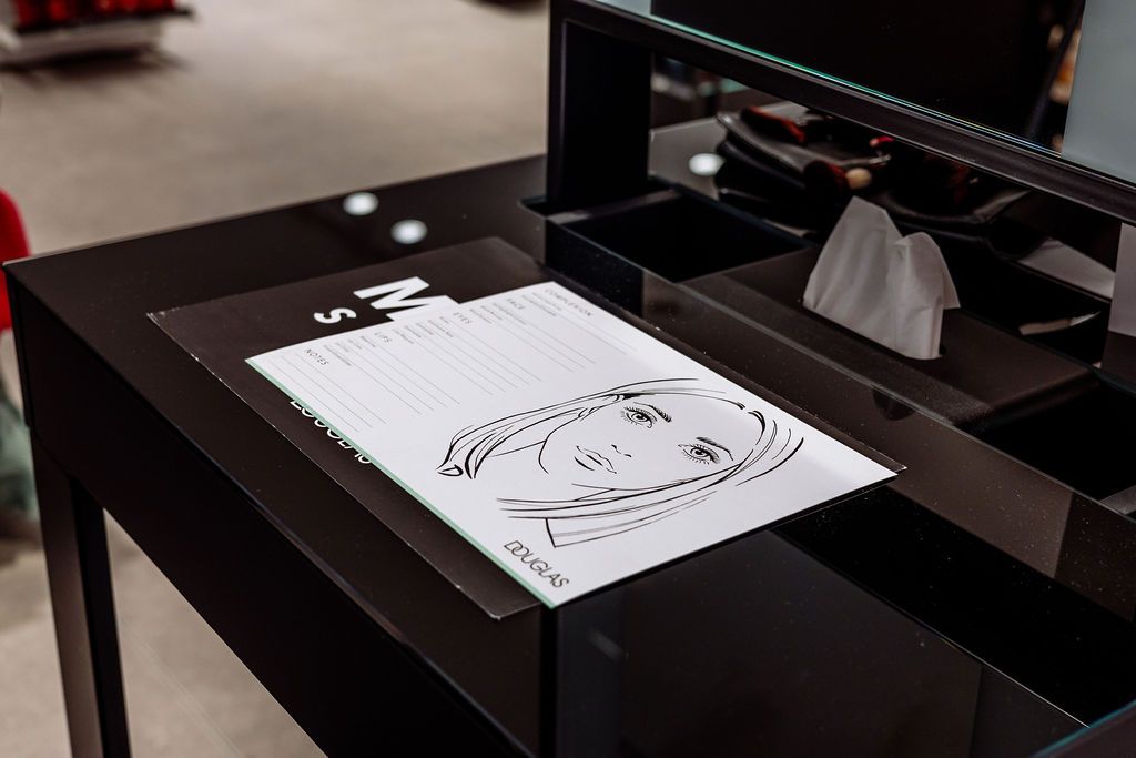 A black and white sketch of a face being drawn on paper with a pen visible in the frame.