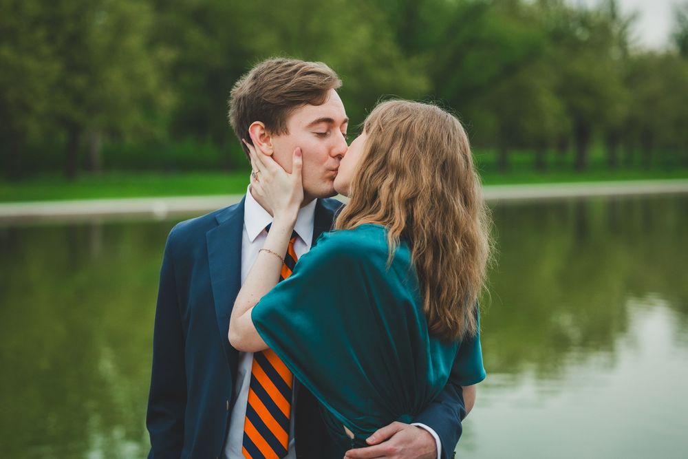 Romantic couple shares a tender kiss by the reflecting pool with lush greenery in the background.