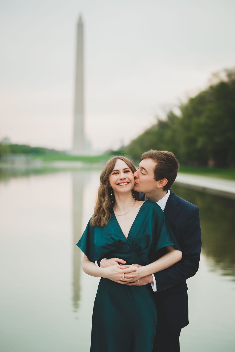 A romantic couple in formal attire embraces by the reflecting pool with the Washington Monument in the background.