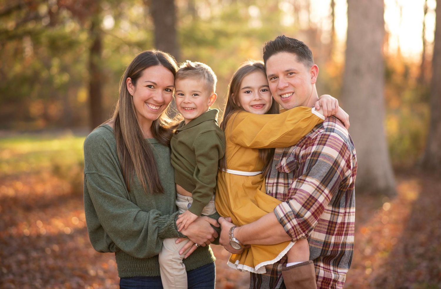 Family wearing coordinated fall outfits embraces outdoors during golden hour autumn photoshoot.