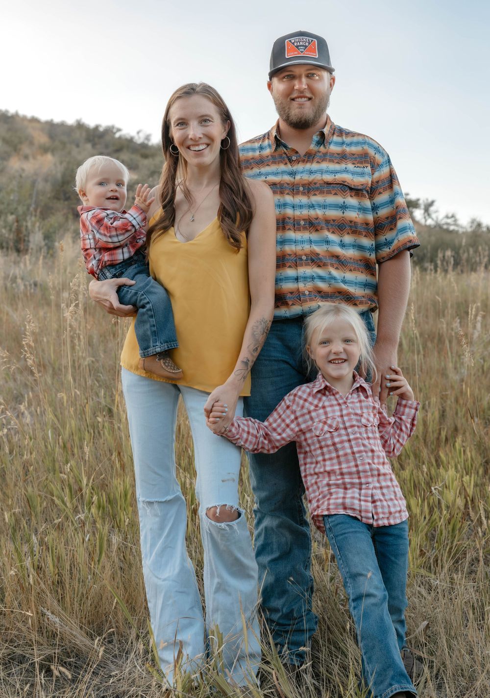 Family group poses together in a golden field during sunset.