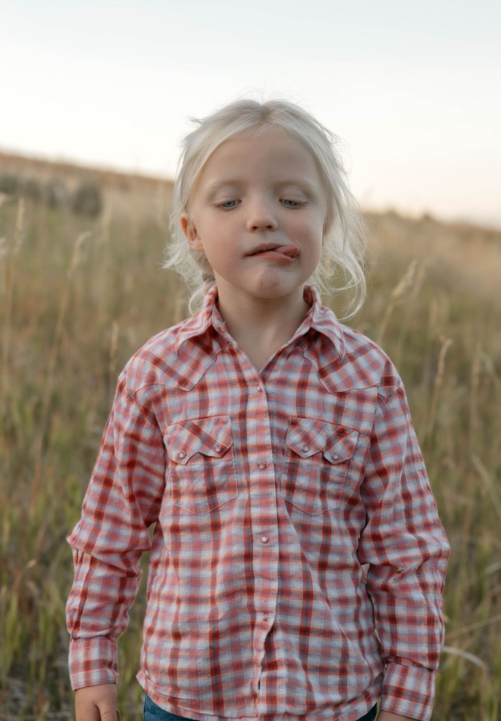 Young child in red plaid shirt smiles while standing in tall grass.