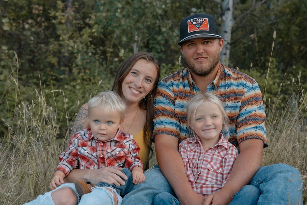 Family in coordinating plaid outfits sitting together in tall grass during outdoor photo session.