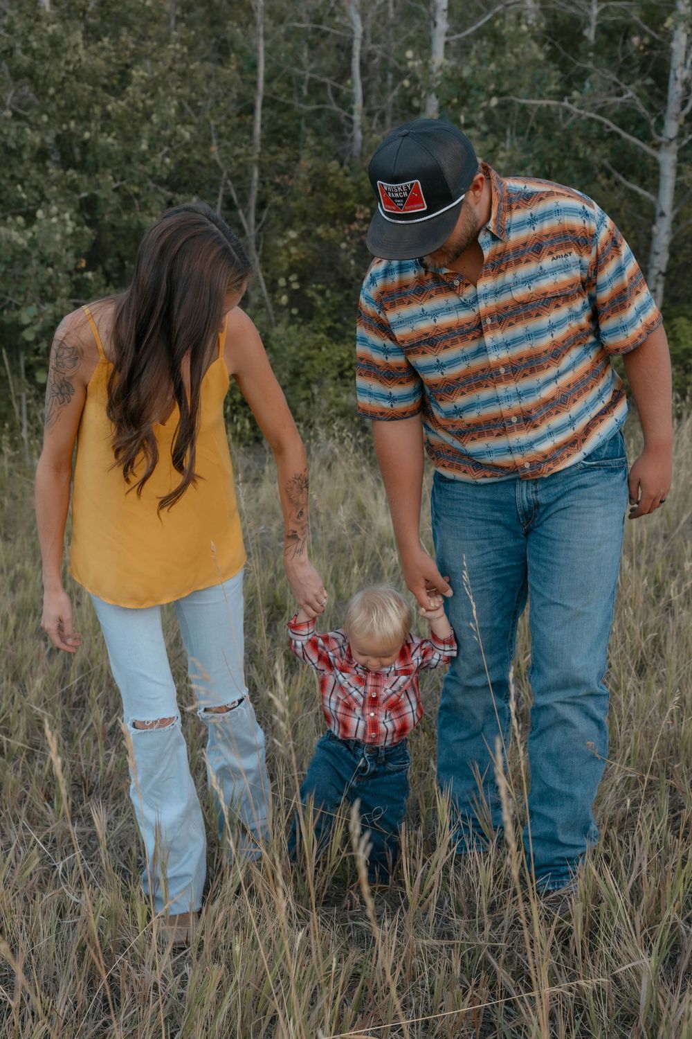 Family walking together through field, wearing casual attire with coordinated plaid.