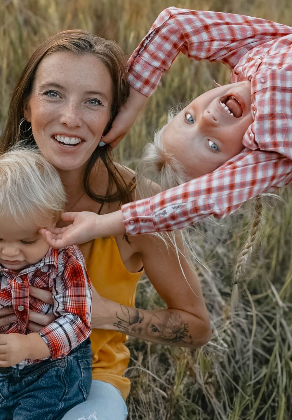 Two people in red gingham and yellow outfits playfully pose in a grassy field.