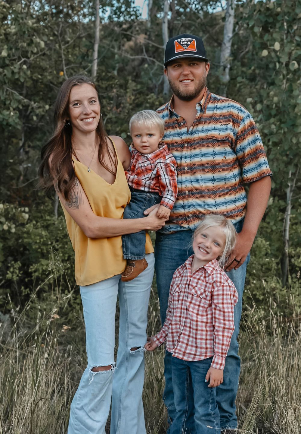 A family group wearing coordinated casual outfits poses together in a natural outdoor setting.