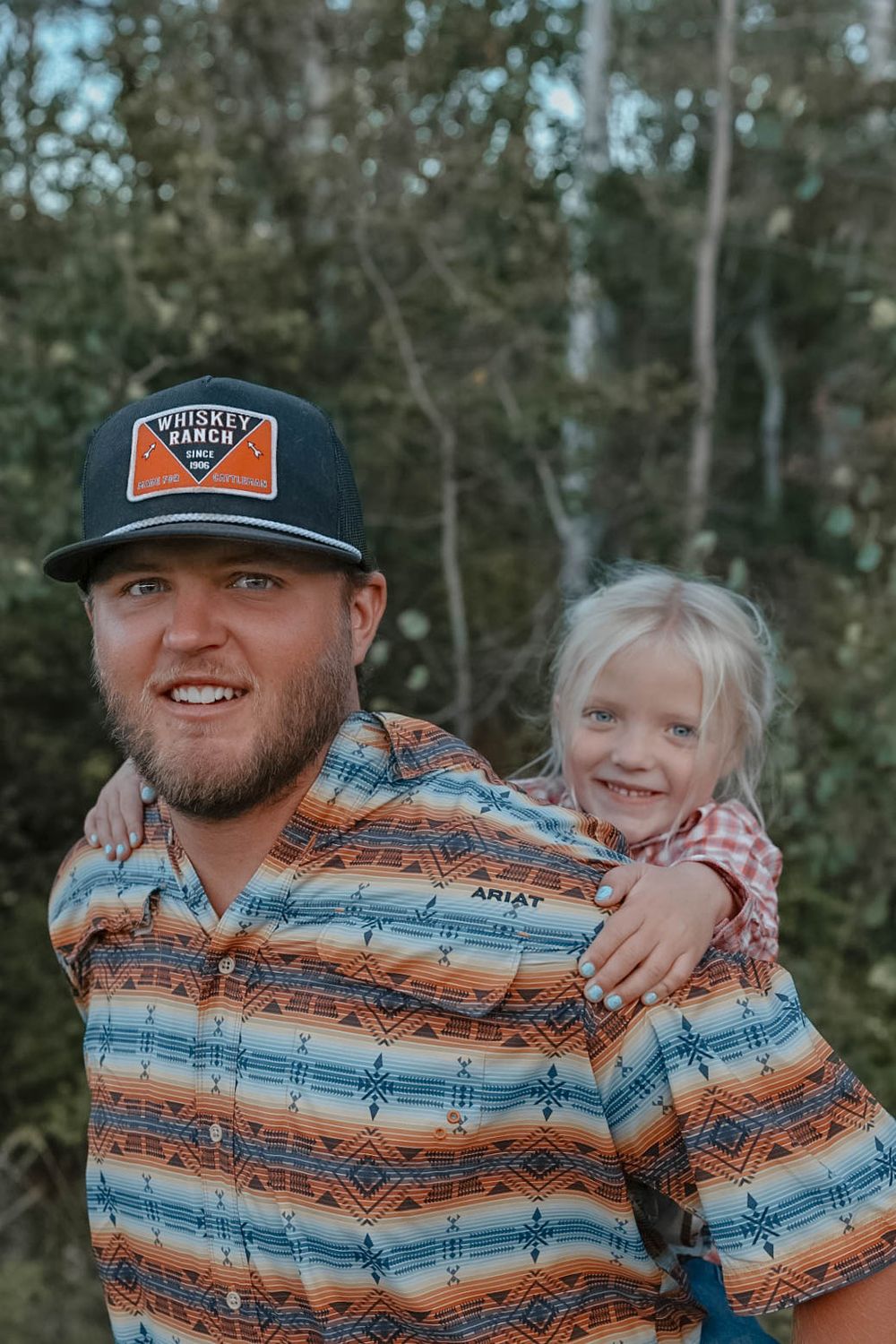 A casual family portrait in an outdoor setting with trees in the background.