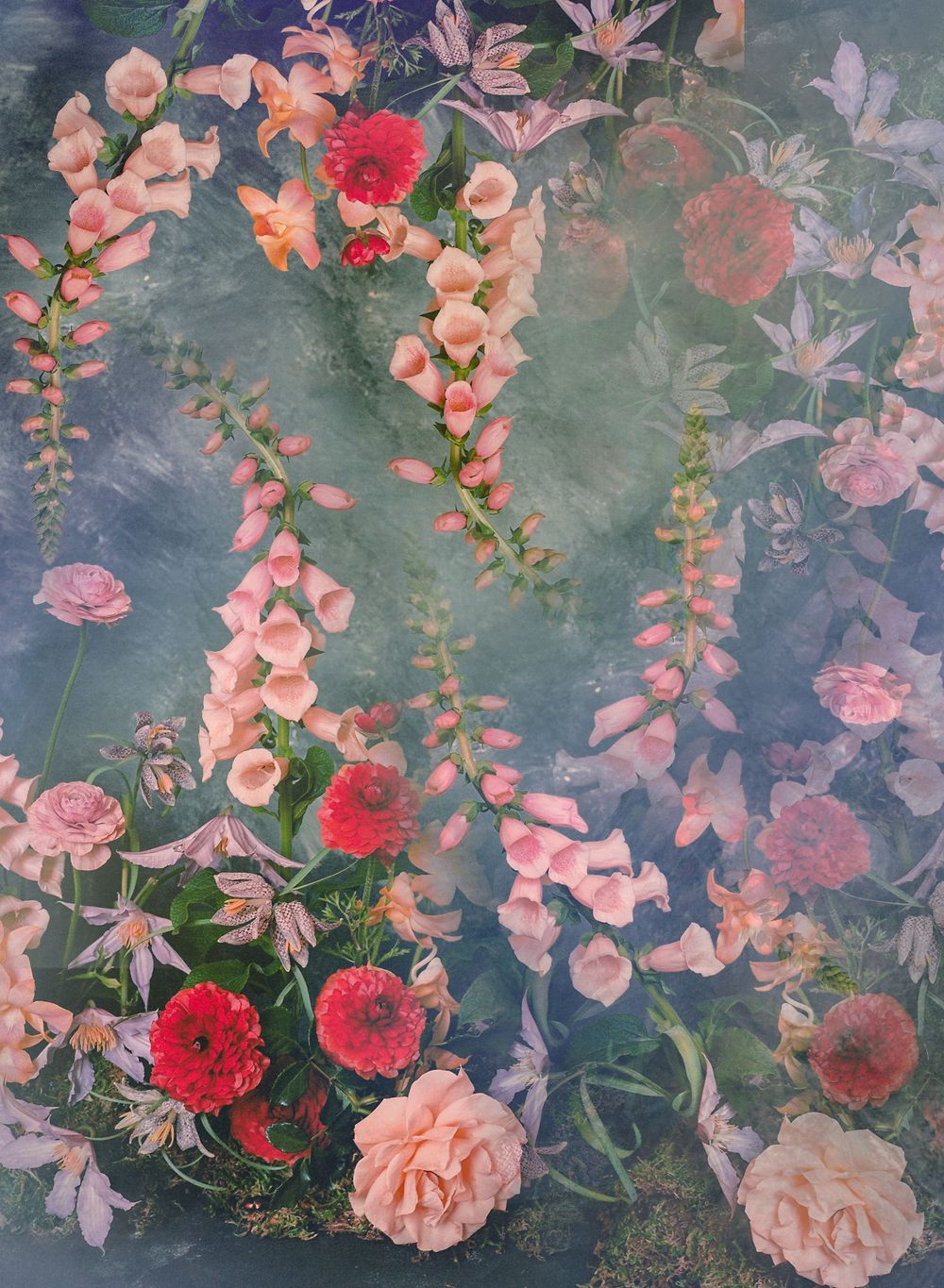 A delicate arrangement of pink and red flowers with green foliage against a muted gray background.