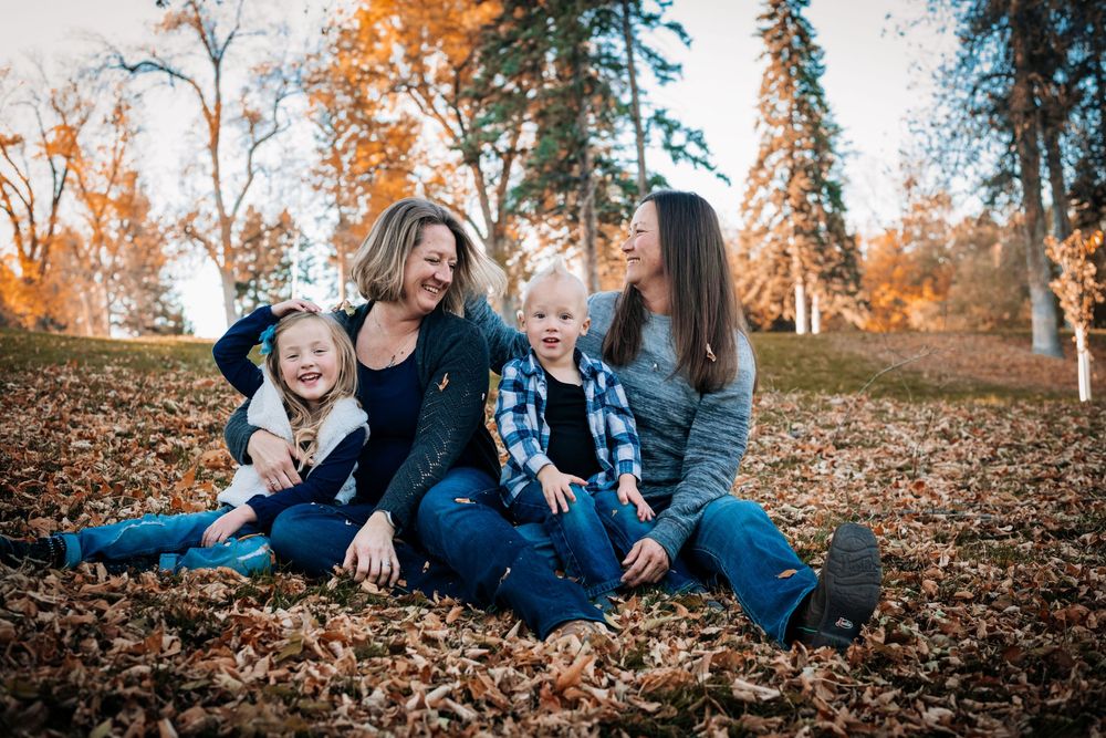 A group sits together in autumn leaves during a fall photo session at sunset.