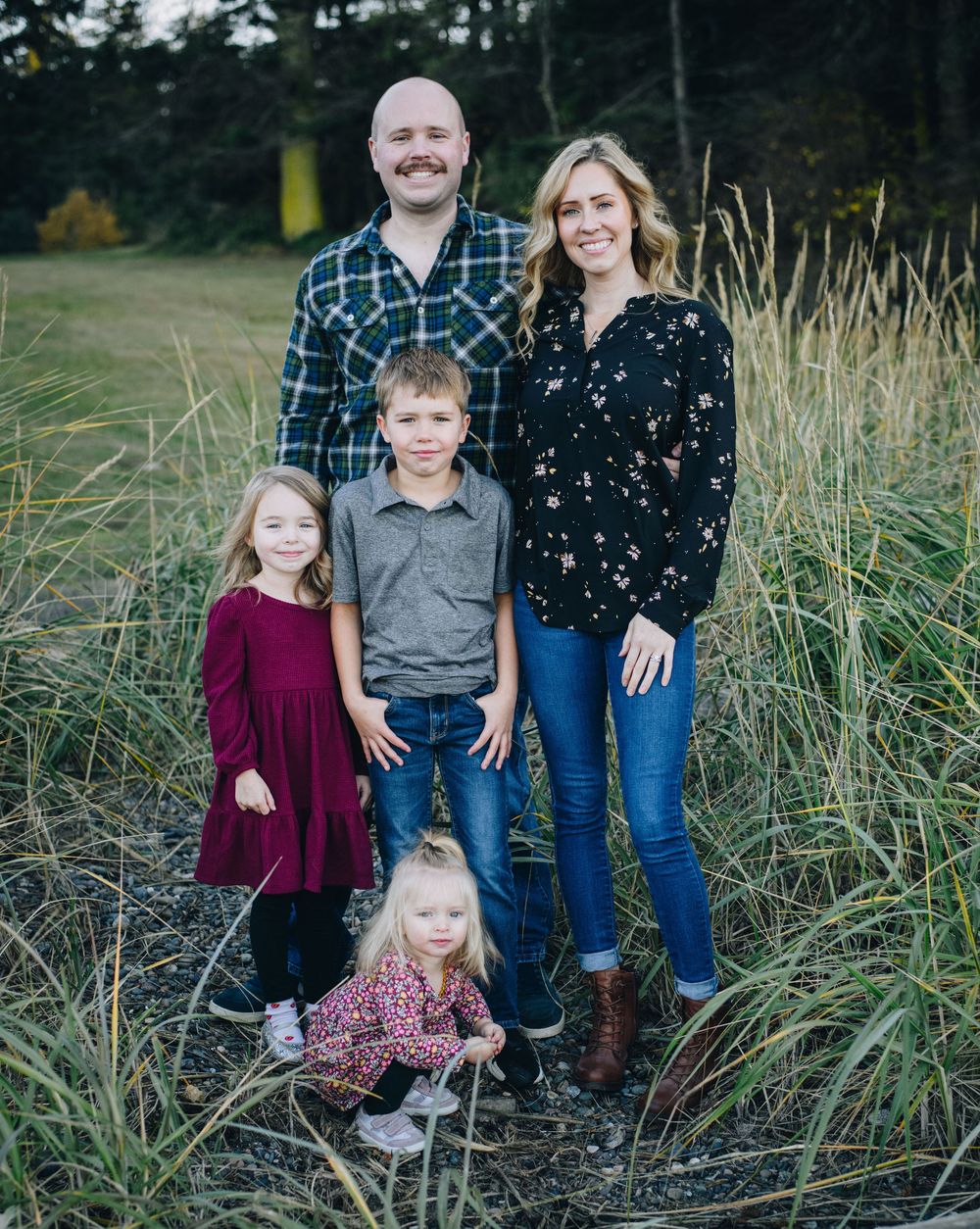 A family poses together outdoors in coordinated casual outfits among tall grasses during a fall photo session.