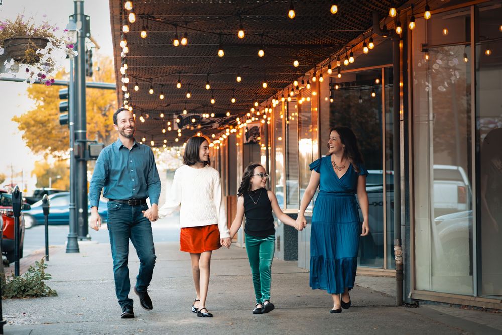 People walking on a sidewalk under string lights at dusk outside storefronts with a warm evening ambiance.