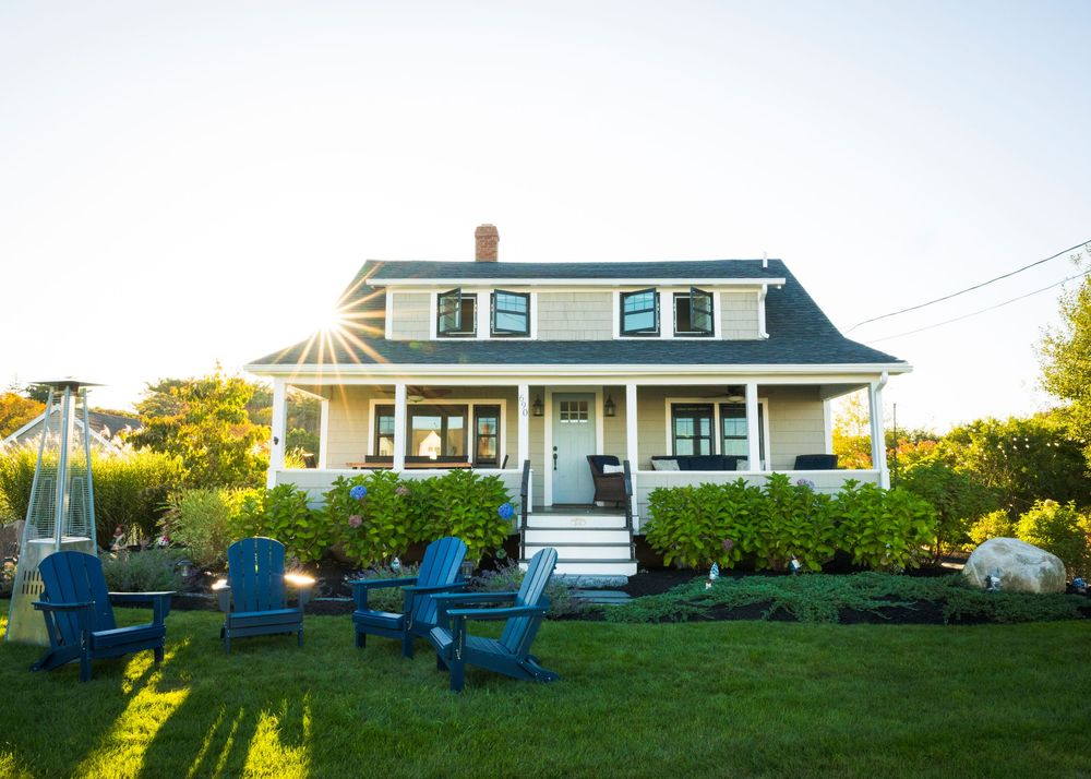 Charming Cape Cod style house with blue Adirondack chairs on the front lawn at sunset.