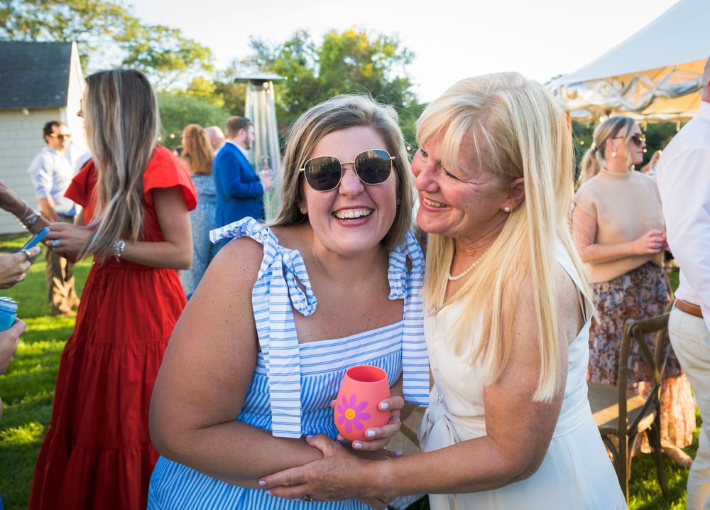 People in summer attire share joyful moments at an outdoor gathering with trees and sunlight in the background.