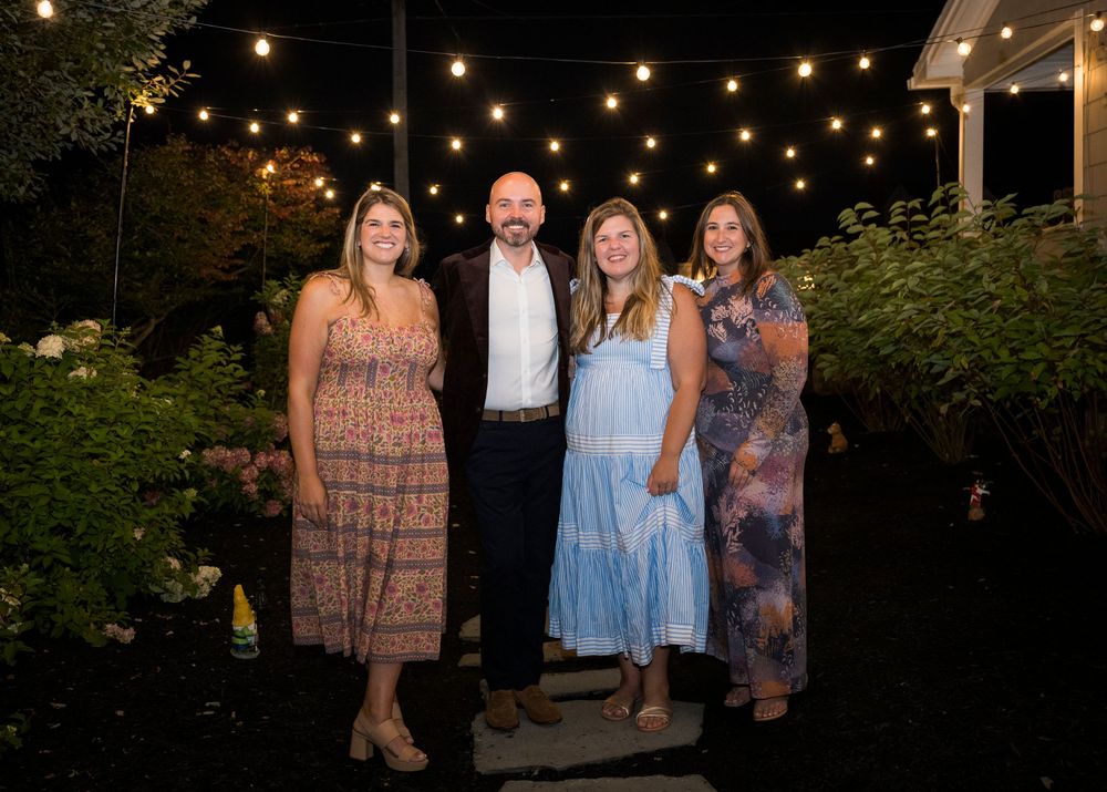 String lights illuminate an outdoor evening gathering with guests in cocktail attire at a social event.