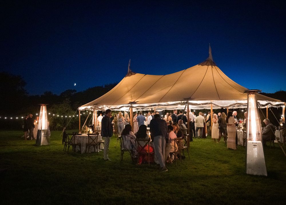 Illuminated wedding tents glow against the dark blue evening sky during an outdoor celebration.