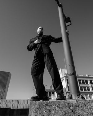 Black and white artistic photo series showing someone in dark clothing standing against a wall with columns in urban setting.