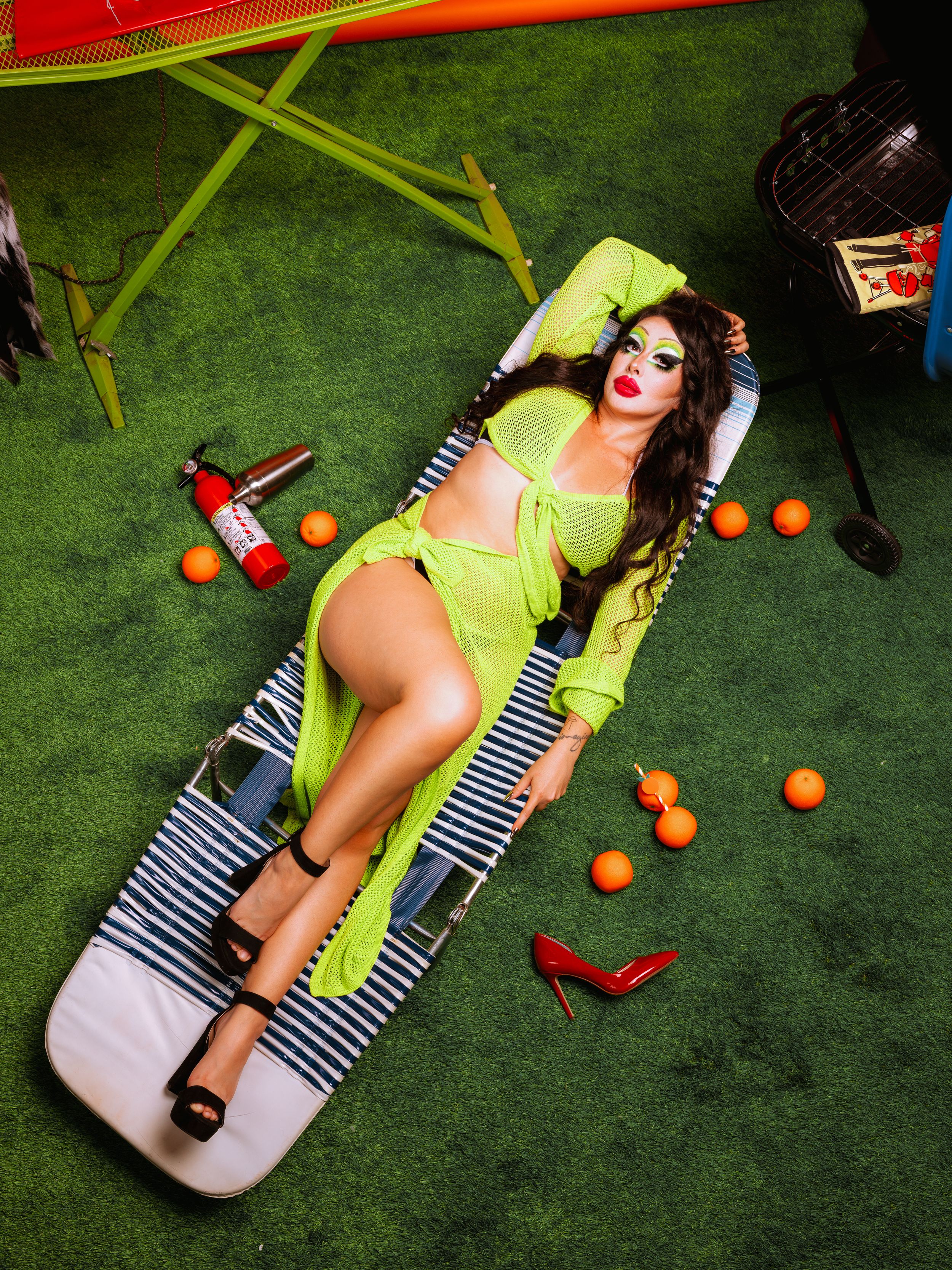 A person in a striped swimsuit lounges on a white surface with scattered oranges and red objects on green turf.