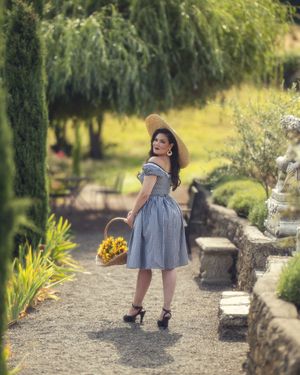 A person in a blue dress and heels walks along a garden path in a series of sequential shots.