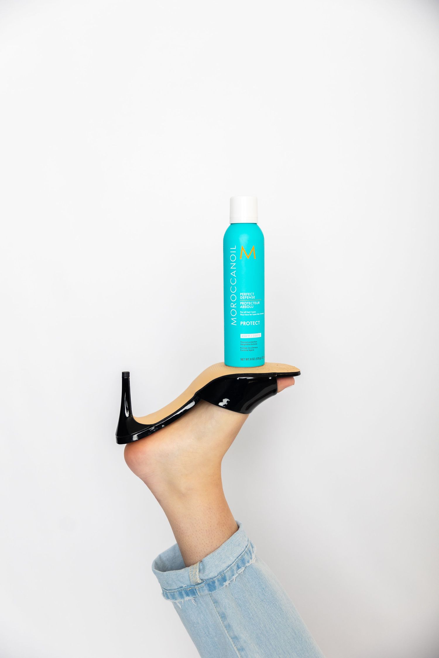 A turquoise can balances precariously on a foot wearing a black high heel shoe and light blue jeans.