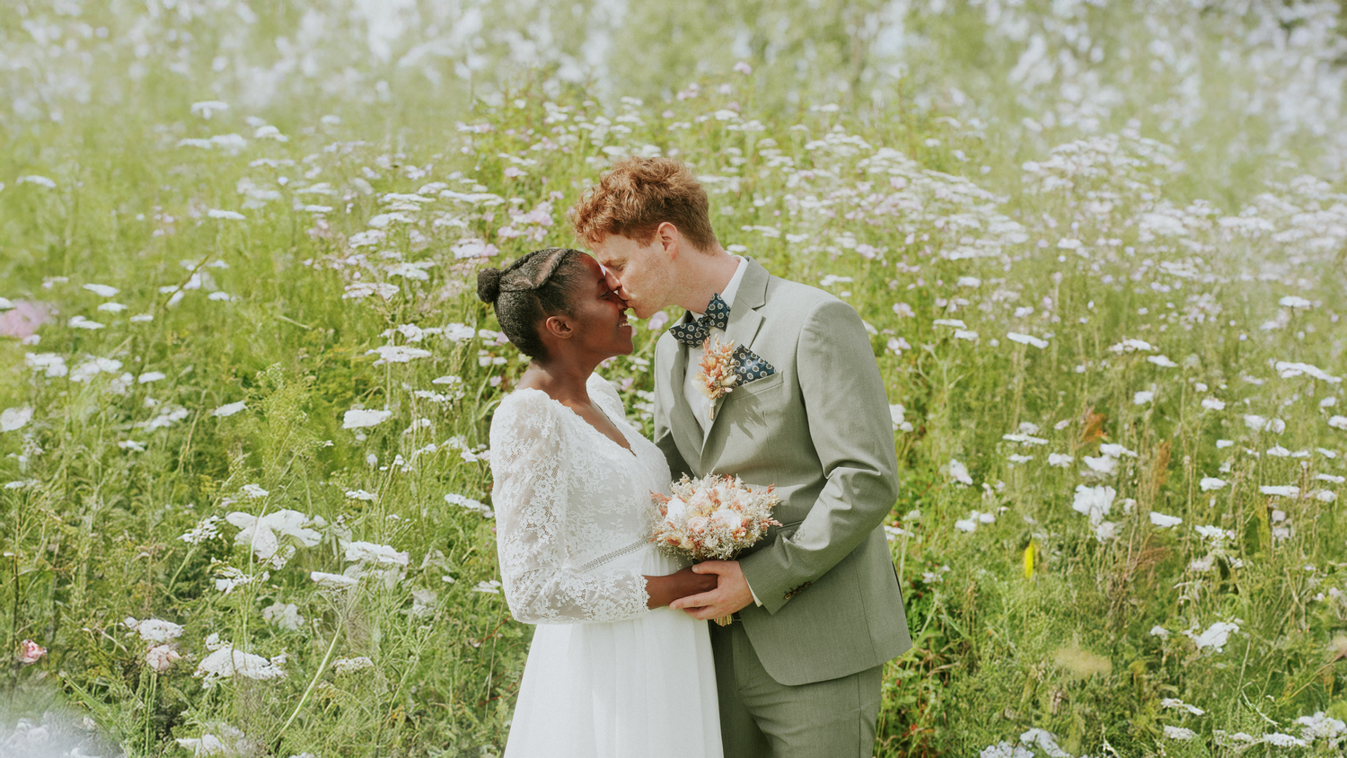 Romantic wedding couple embracing in wildflower meadow with white daisies.
