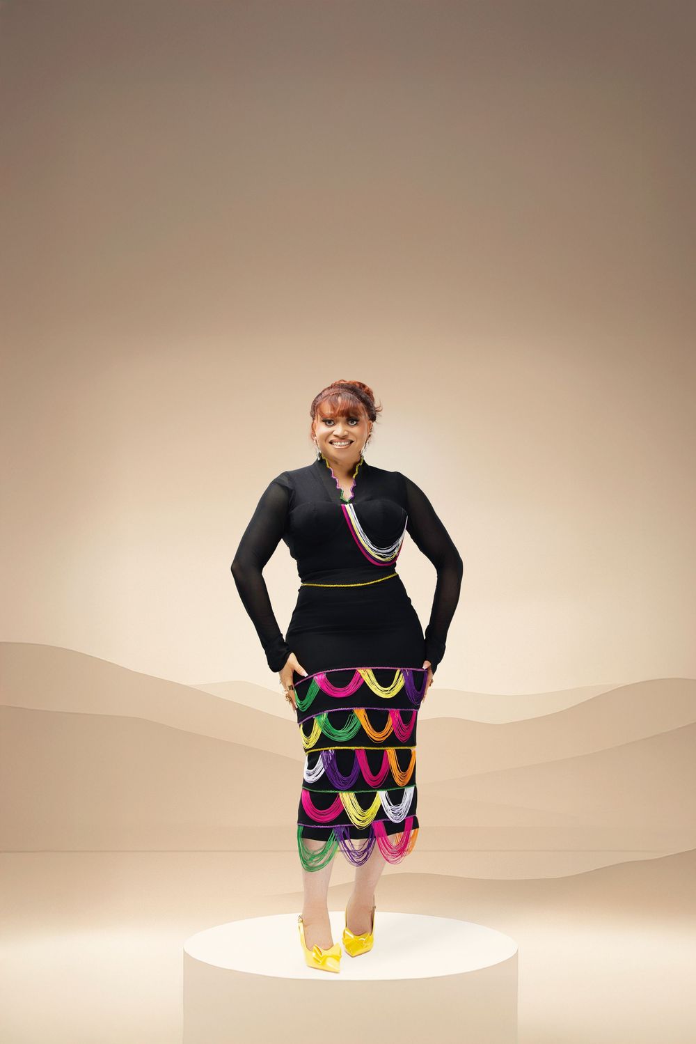 Fashion model poses in black top with colorful wavy pattern skirt against neutral background.