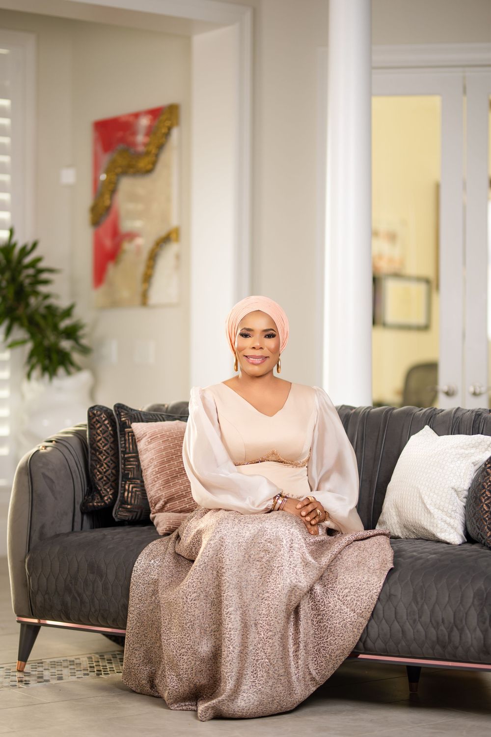 A person in a pink gown lounges elegantly across a grey couch in a bright modern living room.