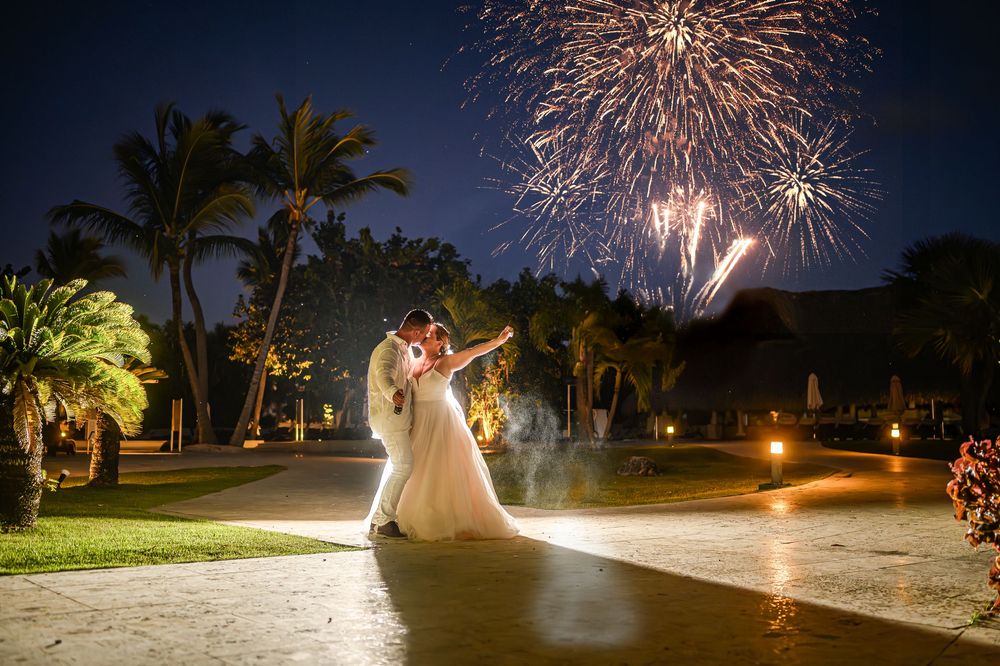Stunning fireworks display illuminates the night sky over a tropical beach setting with palm trees and wedding celebration.