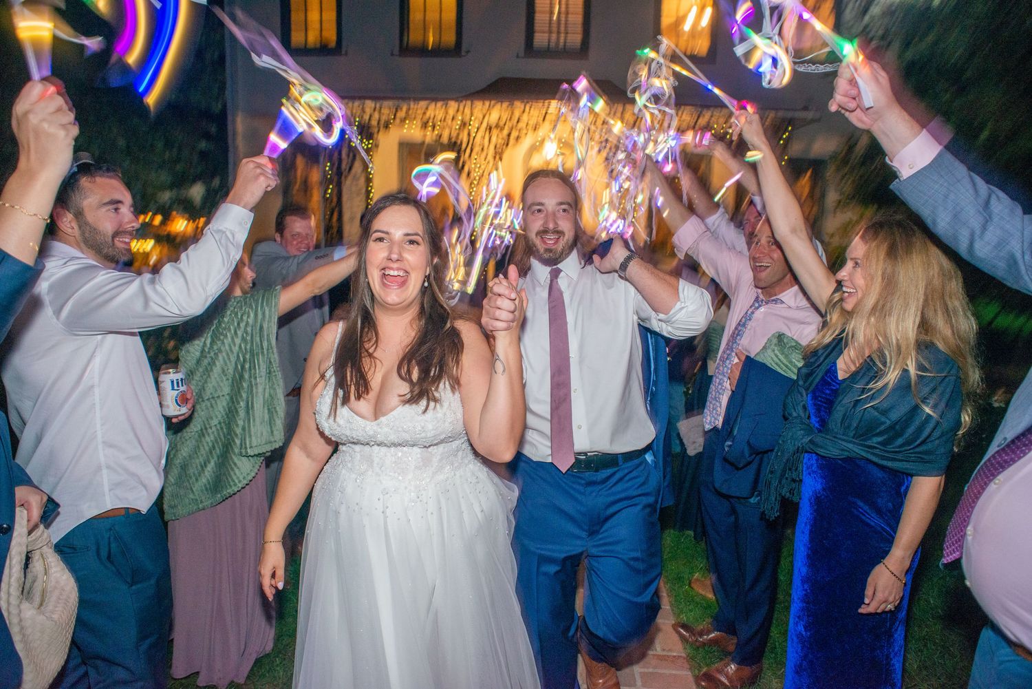 Wedding guests dance and celebrate during an evening reception with colorful lights and festive atmosphere.