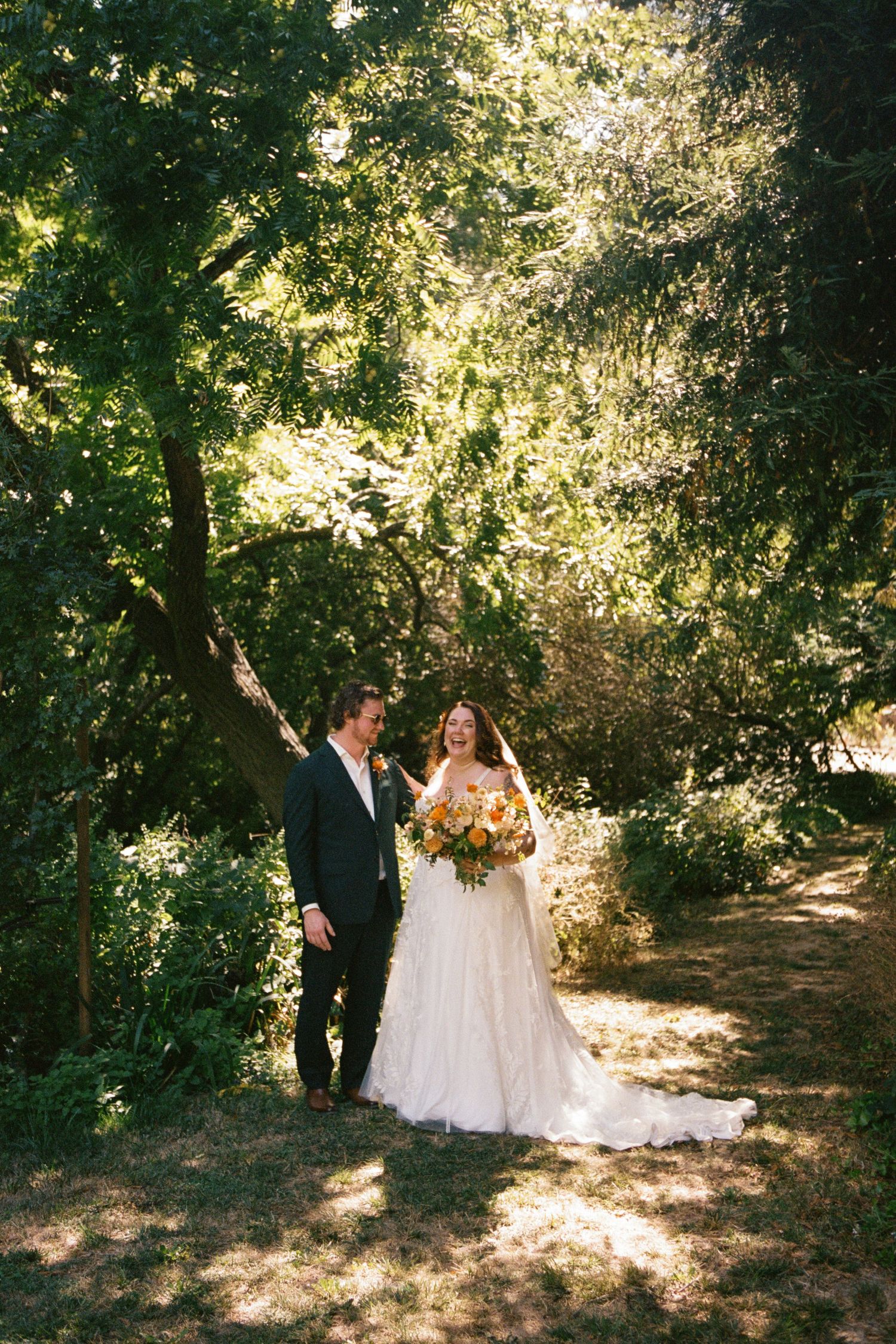 A wooded outdoor wedding scene with dappled sunlight filtering through the trees.