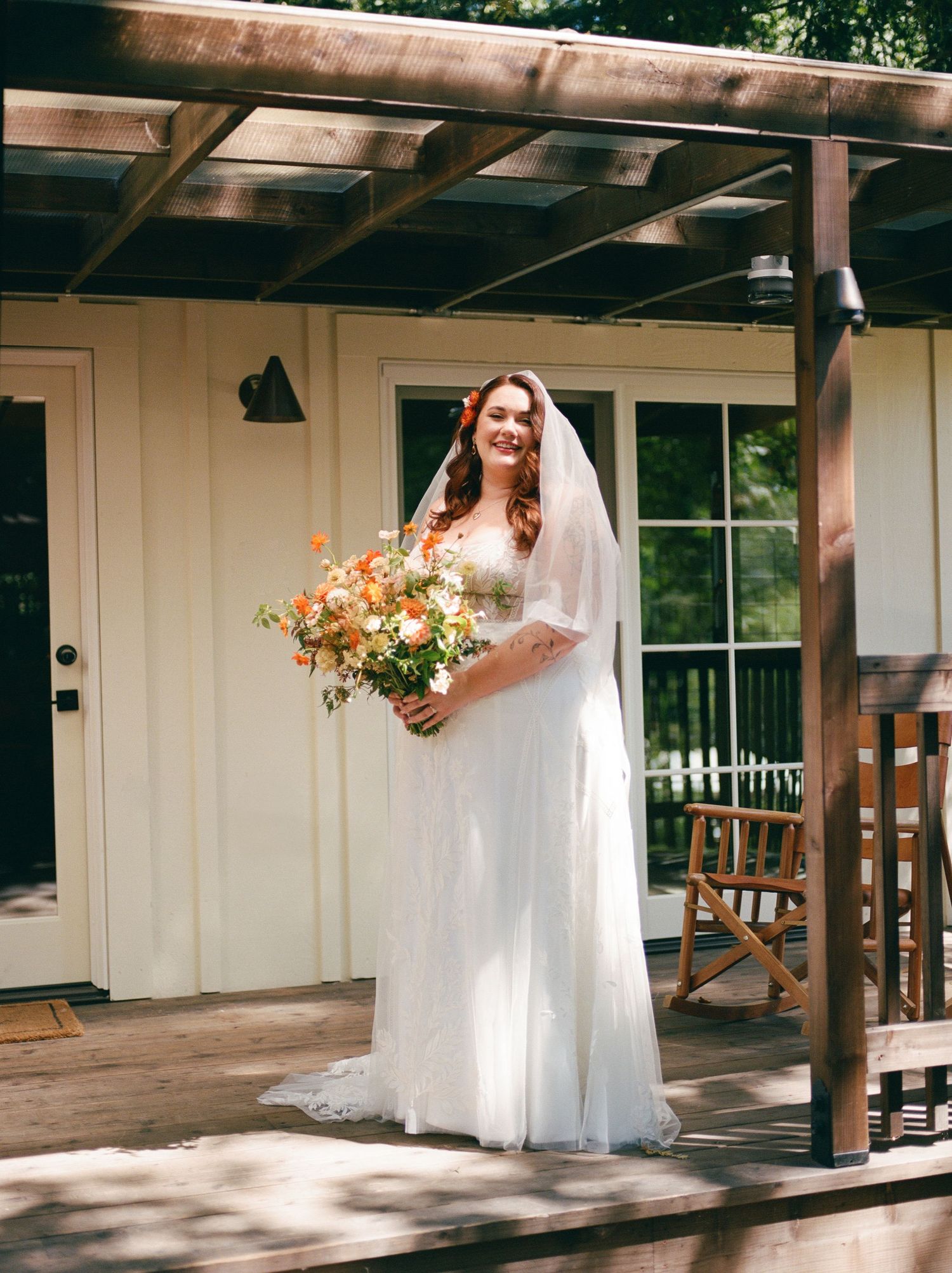A wedding scene on a wooden deck with a person in a white dress holding a vibrant orange bouquet.