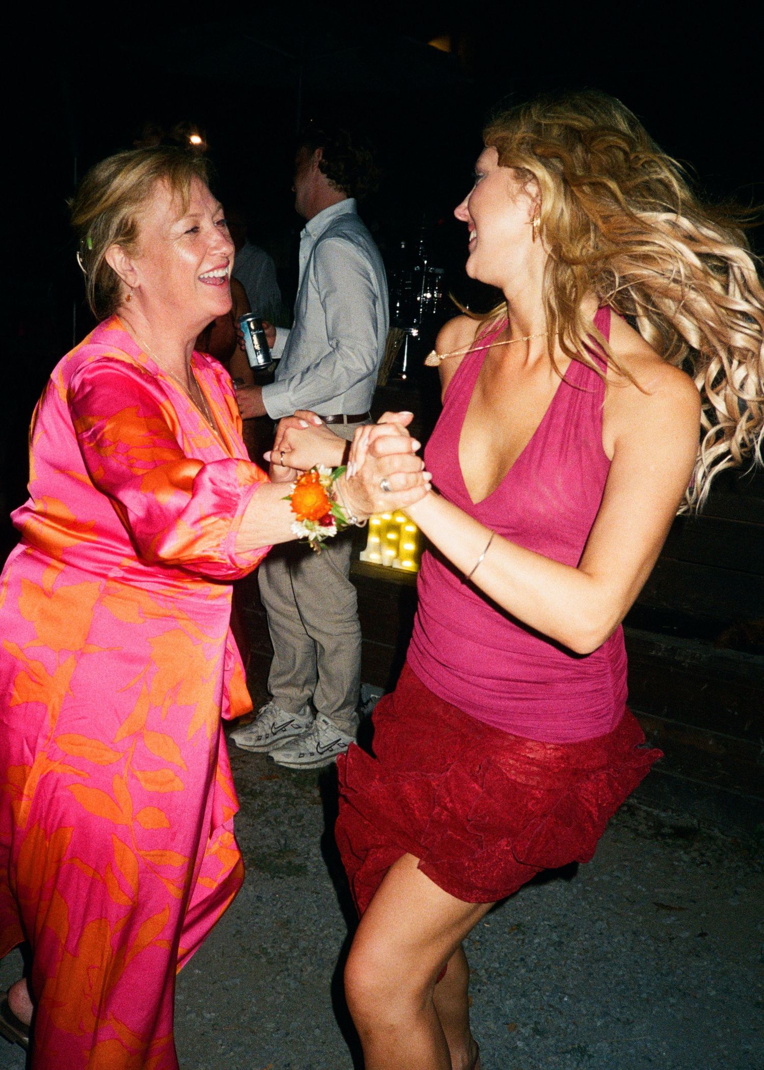 People dancing energetically in bright pink and red outfits at a nighttime party.